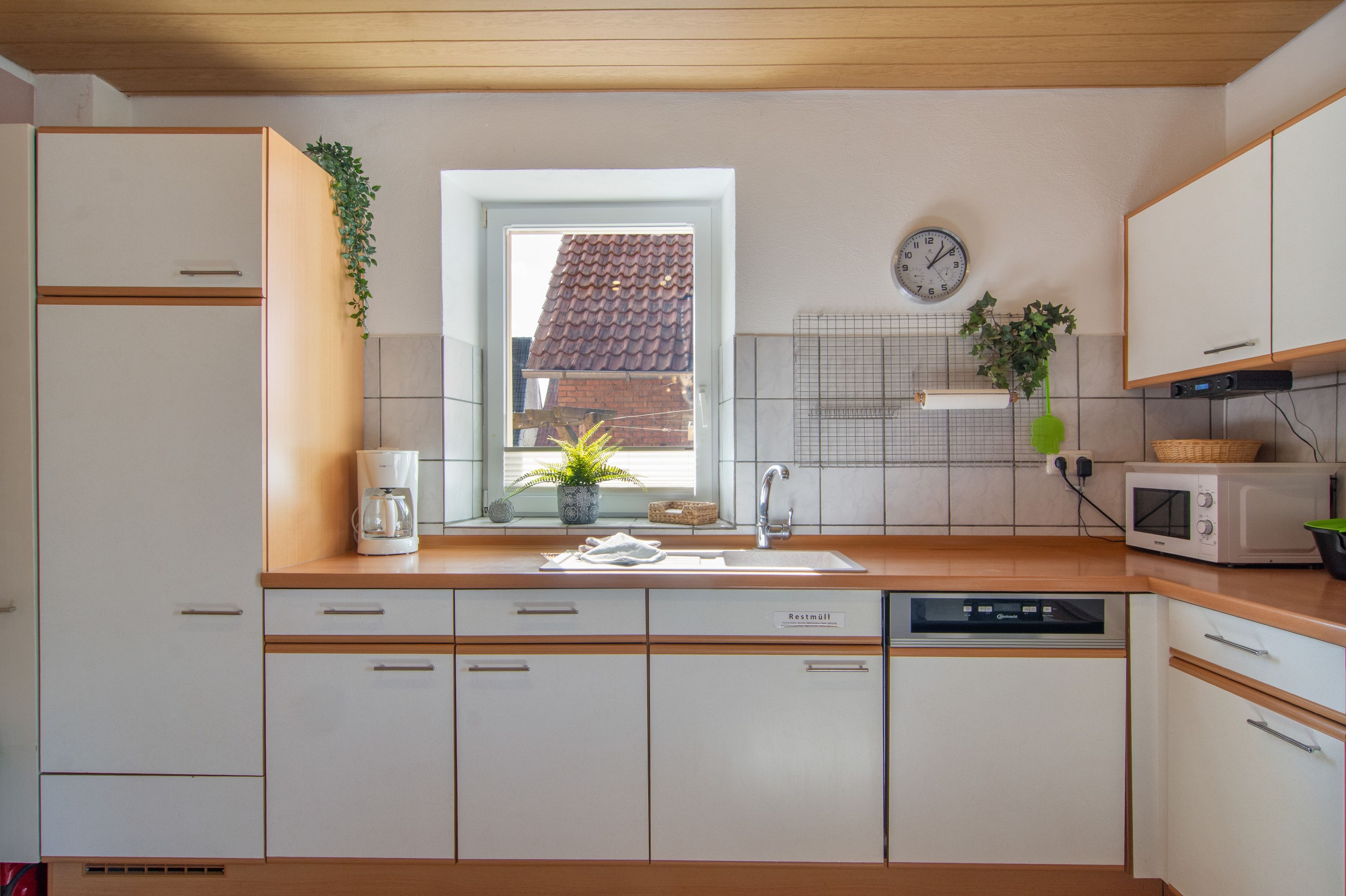 A modern kitchen with a window, a clock, and a microwave.