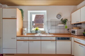 A modern kitchen with a window, a clock, and a microwave. - Holiday Apartment "Fewo 2 - Osterberg" with Private Terrace, Shared Garden & Wi-Fi (Liebenau)