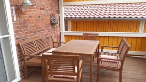 A wooden deck with a table and chairs, a brick wall, and a yellow fence. - Holiday Apartment "Fewo 2 - Osterberg" with Private Terrace, Shared Garden & Wi-Fi (Liebenau)