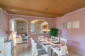 Comedor con techo de madera, sillas blancas y una mesa preparada para cuatro.