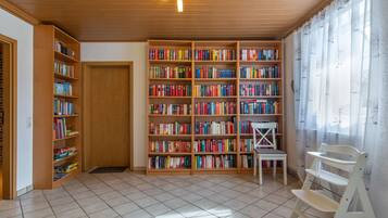 A room with a large bookshelf filled with books, a wooden door, and a tiled floor.