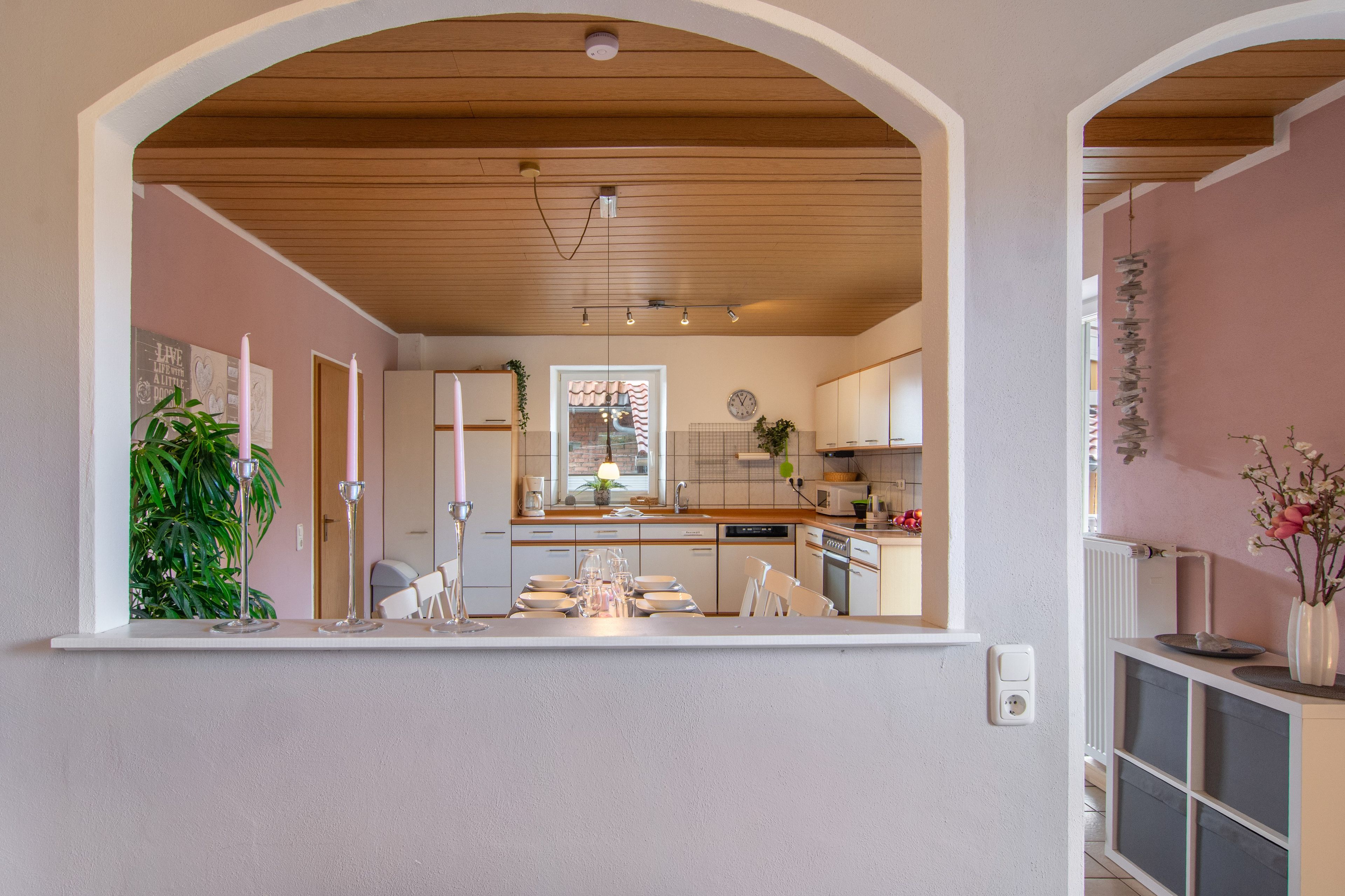 Een moderne keuken met een houten plafond, witte kastjes, en een eethoek met stoelen en een tafel gedekt voor vier personen.
