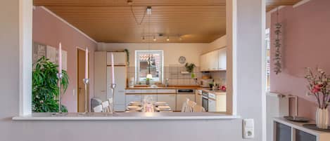 A modern kitchen with wooden ceiling, white cabinets, and a dining area with chairs and a table set for four.