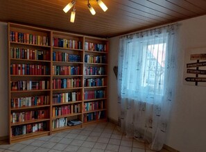 A library with wooden bookshelves filled with books, a tiled floor, and a window with a floral curtain.