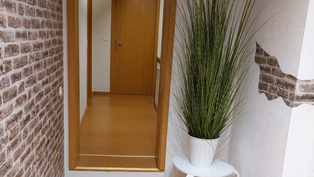 A hallway with a brick wall, a wooden door, and a potted plant on a white stool. - Holiday Apartment "Fewo 2 - Osterberg" with Private Terrace, Shared Garden & Wi-Fi (Liebenau)