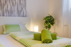 A neatly made bed with striped bedding, a green plant in a white pot, and a headboard with a wooden texture. - Holiday Apartment "Fewo 2 - Osterberg" with Private Terrace, Shared Garden & Wi-Fi (Liebenau)