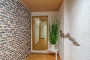 Un pasillo con pared de ladrillo, techo de madera, una puerta blanca y una planta en maceta.