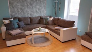 Een woonkamer met een hoekbank, een kleine ronde tafel en een behang met patroon.