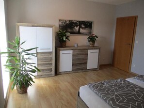 Une chambre à coucher avec un lit, une armoire en bois, un petit meuble blanc, un tableau et une plante en pot.