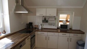 Een keuken met houten aanrechtbladen, een vaatwasser, een fornuis, kastjes, een magnetron en een raam.