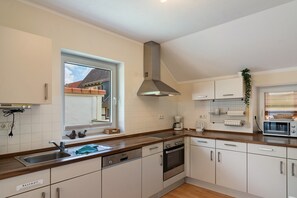 A modern kitchen with a dishwasher, oven, and a window with a view of a house.