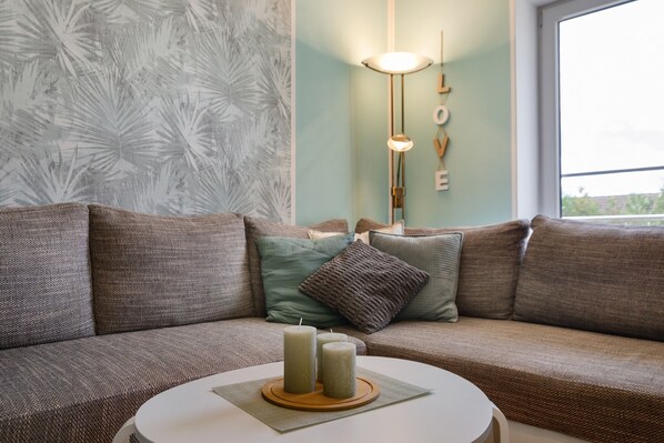 A modern living room with a sectional sofa, a round coffee table with candles, and a wall with a 'LOVE' decoration.