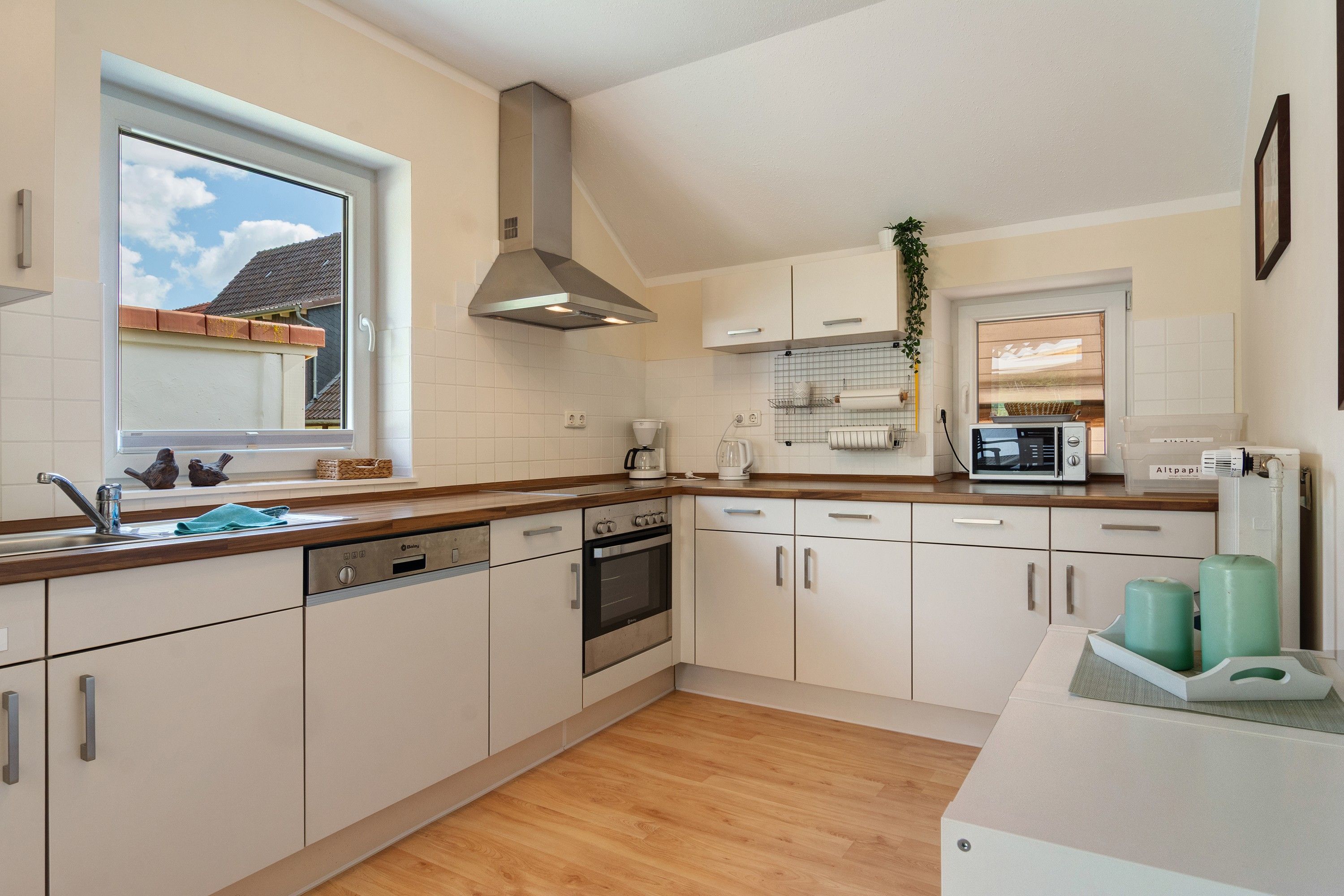 A modern kitchen with white cabinets, a stainless steel range hood, a built-in oven, and a microwave.
