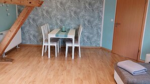 Een kamer met een houten balk, een tafel met stoelen, een behang met patroon, een deur en een bed met een opgevouwen handdoek.