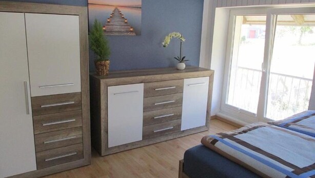 Een slaapkamer met een bed, een kledingkast, een nachtkastje met een plant en een raam met uitzicht.