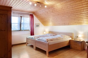 A bedroom with a wooden ceiling, a bed with floral bedding, a nightstand with a lamp, and a window with a view of trees.