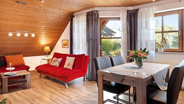 Una habitación acogedora con un sofá rojo, una mesa de comedor y vistas al exterior.
