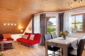 A cozy room with a red sofa, a dining table, and a view of the outdoors.