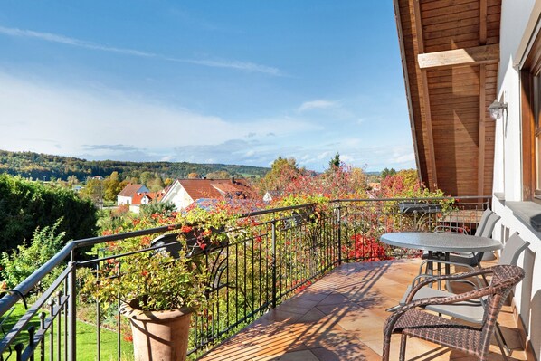 A balcony with a view of a village, a table, and chairs.