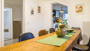 Un coin repas avec une table en bois, des chaises, un vase de fleurs et une cuisine en arrière-plan.