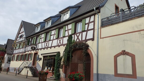 Un bâtiment traditionnel à colombages, doté d’un escalier, d’une grande porte en bois et de jardinières placées sur le trottoir.