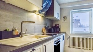 Une cuisine équipée d’un évier, de placards, d’une fenêtre donnant sur un paysage agréable et d’un radiateur.
