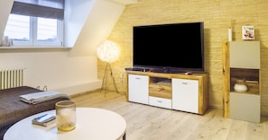 A modern living room with a flat-screen TV, wooden cabinets, a round table, and a floor lamp.