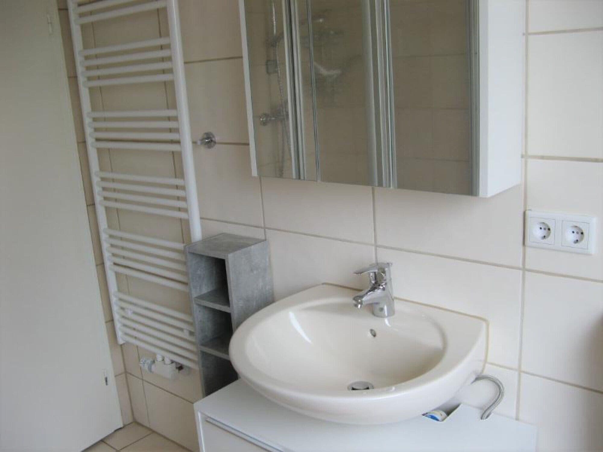 Een badkamer met een wit wastafel, een spiegel erboven en een handdoekrek aan de linkerkant.
