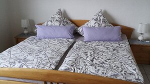 Un lit double avec une couvre-lit à motifs floraux, deux oreillers, une table de chevet avec une lampe et un tableau représentant des fleurs blanches accroché au mur.