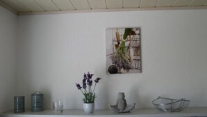 Une étagère avec une plante en pot, une figurine en céramique, un panier en fil de fer et un tableau encadré représentant des plantes.