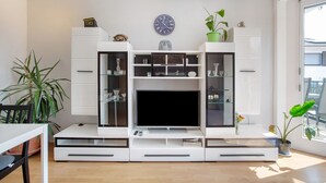Una sala moderna con televisor de pantalla plana, estanterías empotradas y una planta en maceta.