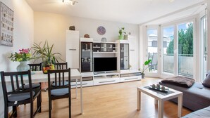 Una sala de estar moderna con un televisor de pantalla plana, sillas de madera, una mesa de comedor y un sofá.