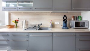 Una cocina moderna con armarios grises, un lavamanos de acero inoxidable, un microondas y una cafetera.