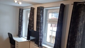 Ein Zimmer mit Schreibtisch, Stuhl und einem Vorhangfenster.