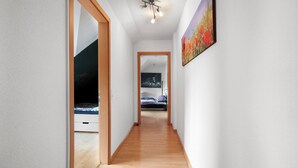 A hallway with wooden flooring, white walls, and a ceiling light fixture.