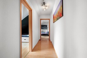 A hallway with wooden flooring, white walls, and a ceiling light fixture.