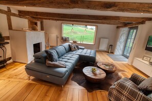 Un salon moderne avec un canapé d’angle, une cheminée, une grande fenêtre offrant une belle vue et un plancher en bois.