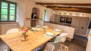 Une cuisine moderne avec des meubles blancs, une table à manger en bois pour quatre personnes et une grande fenêtre donnant sur un paysage verdoyant.