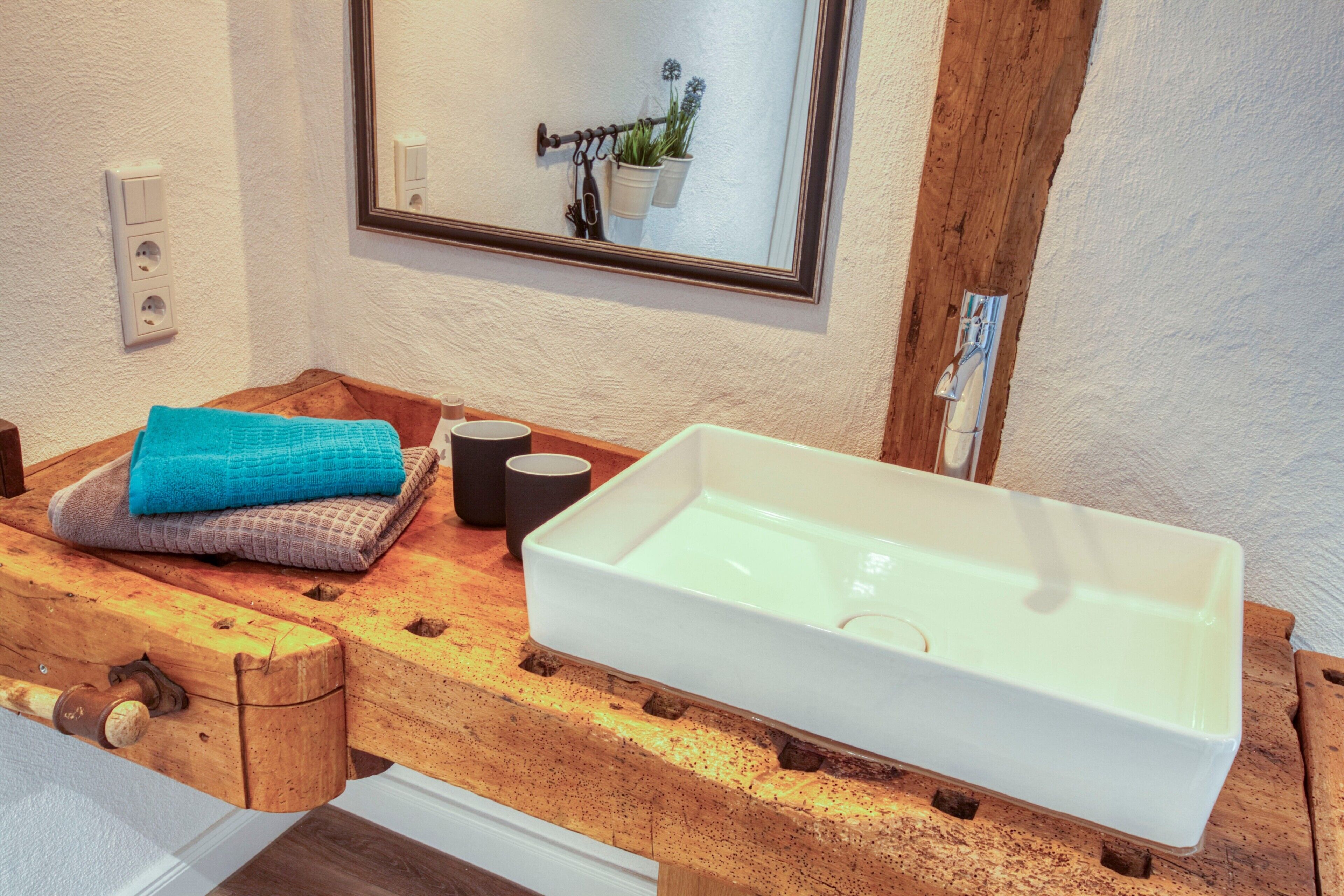 A bathroom with a wooden vanity, a white sink, and a mirror above it.