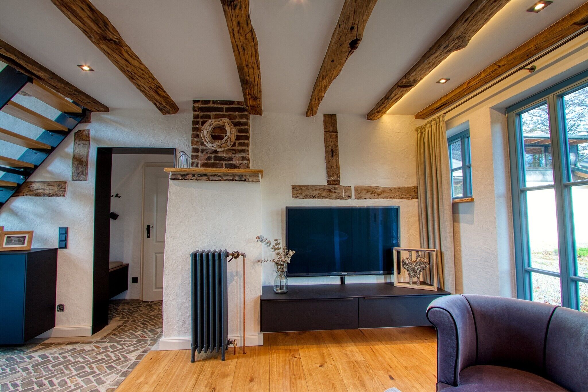 Une pièce avec des poutres apparentes, une cheminée en pierre, une grande fenêtre et un banc intégré.