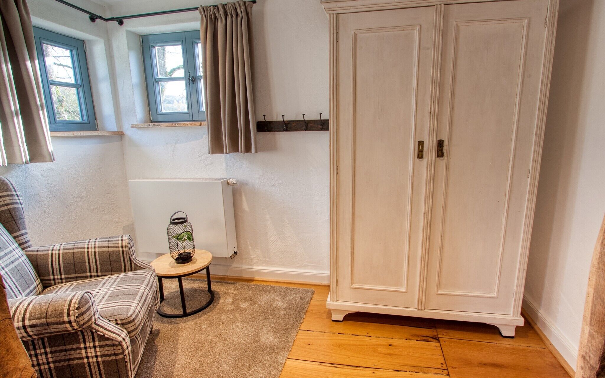 Une pièce avec un canapé à carreaux, une petite table ronde ornée d’une plante, une armoire blanche et un radiateur.