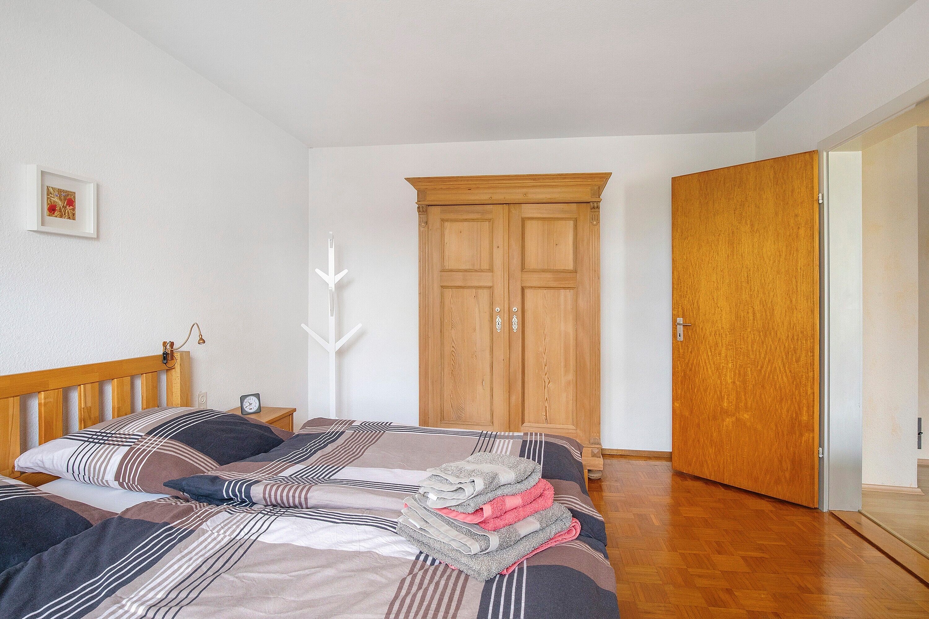 Une chambre à coucher avec un lit en bois, une armoire en bois, une table de chevet avec une lampe et un tableau encadré au mur.