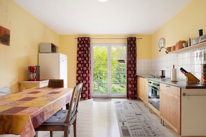 A kitchen with a dining table, chairs, a microwave, a refrigerator, and a window with curtains.