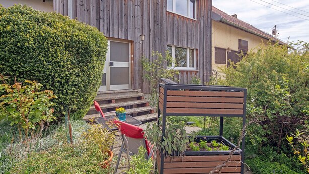 A wooden house with a garden, a wooden chair, and a red chair.