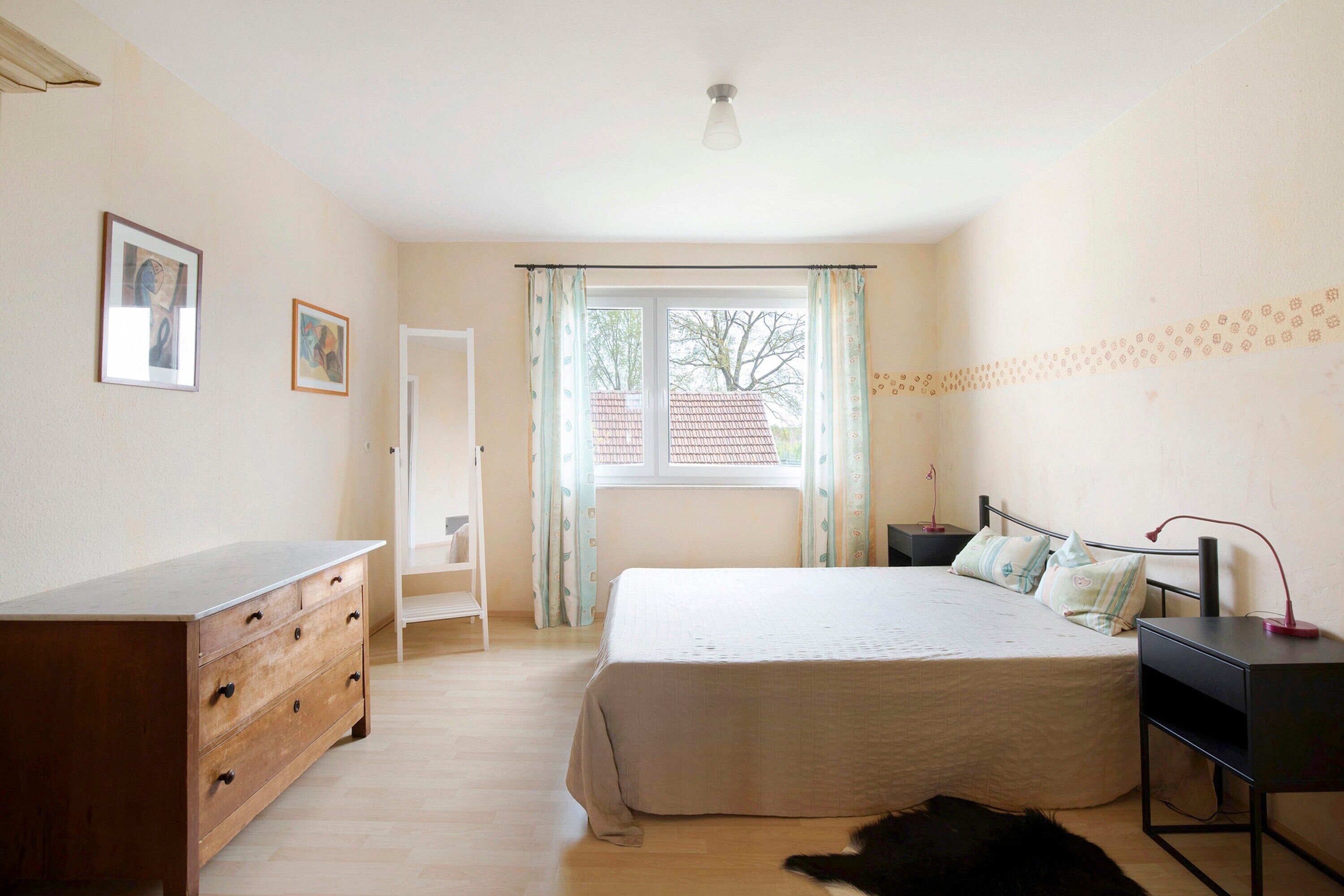 A bedroom with a bed, dresser, nightstand, and a window with curtains.