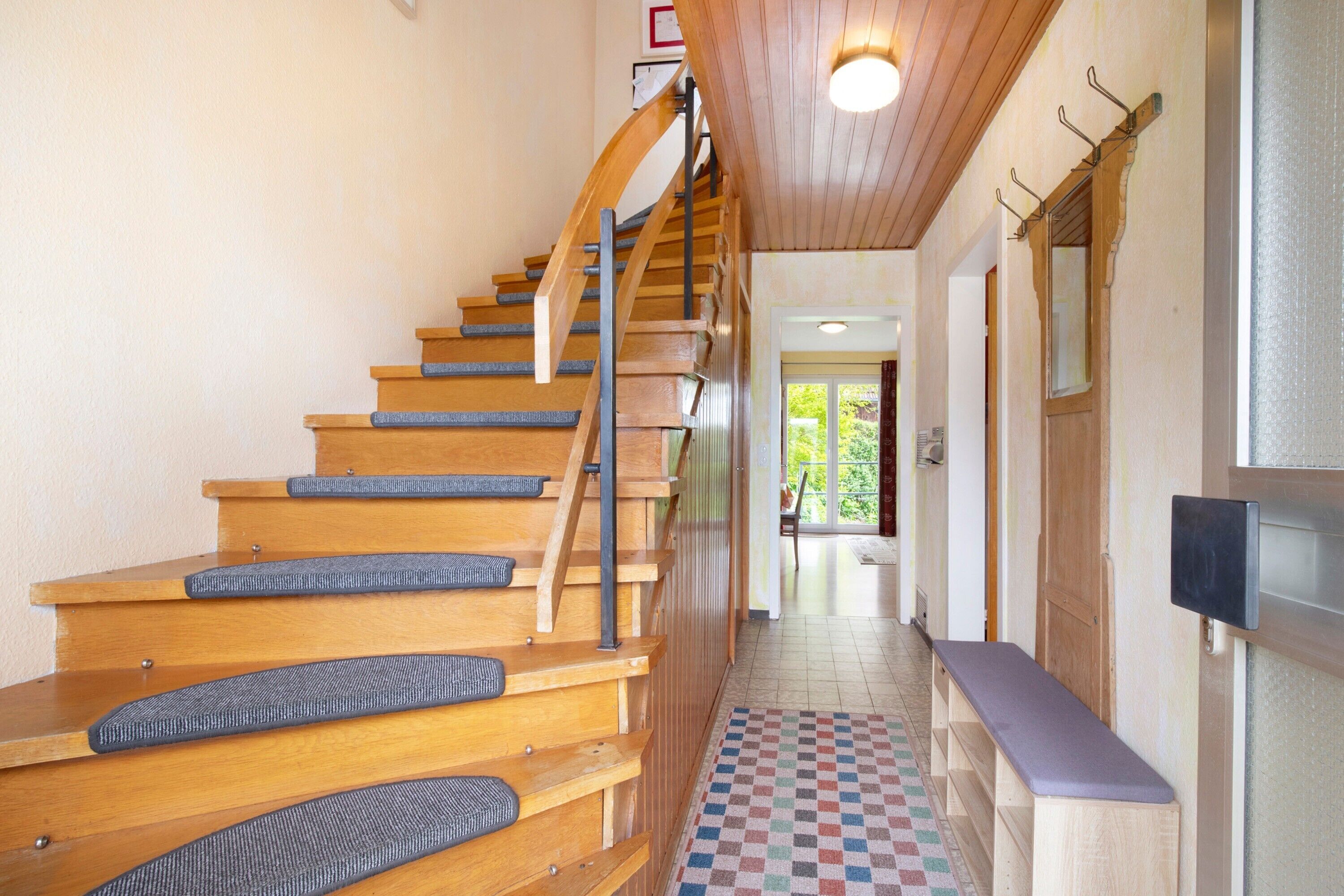 Una escalera de madera con un tapete de piso a cuadros, un banco y una puerta con ventanal.