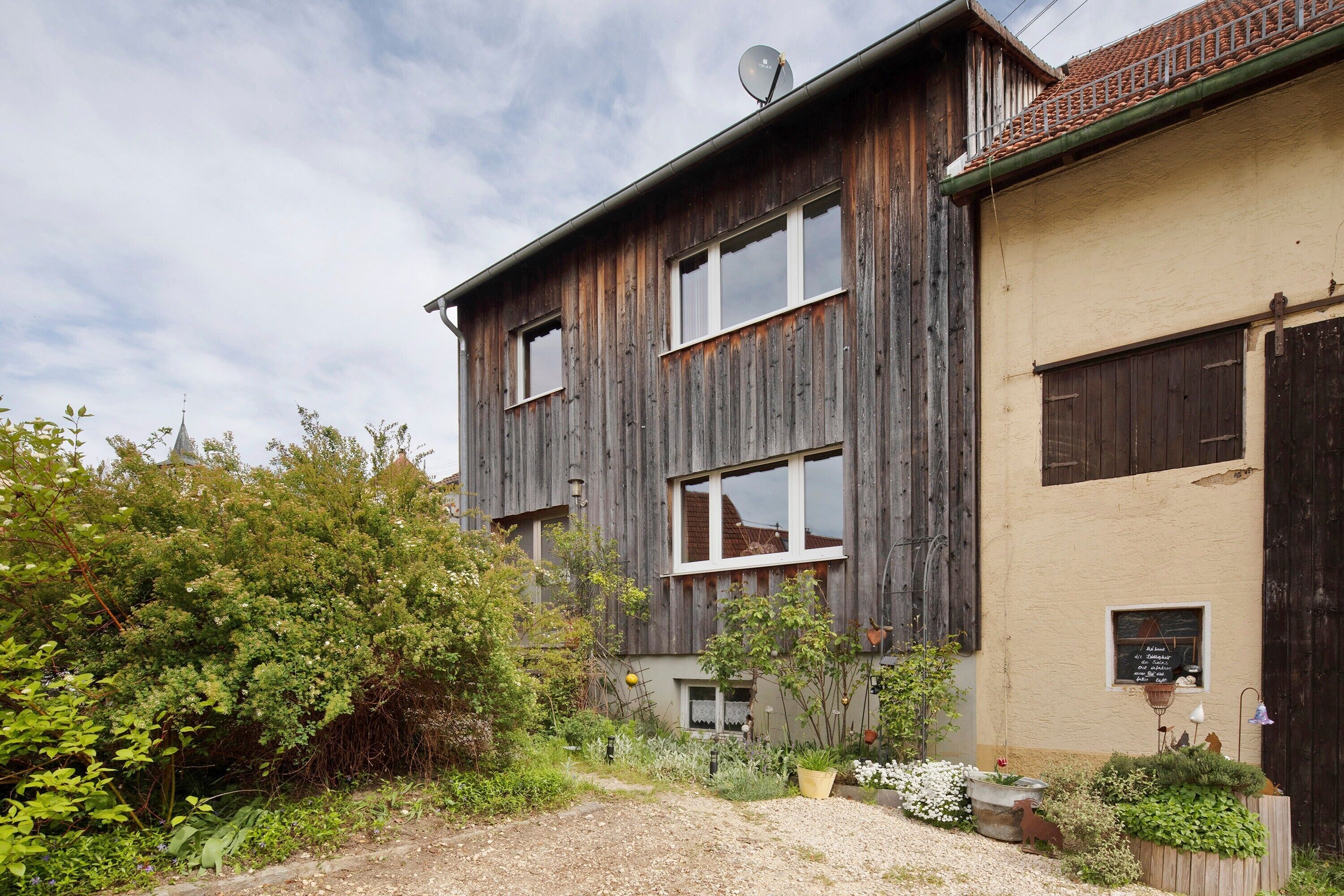 A rustic building with a dirt path, wooden fence, and greenery.