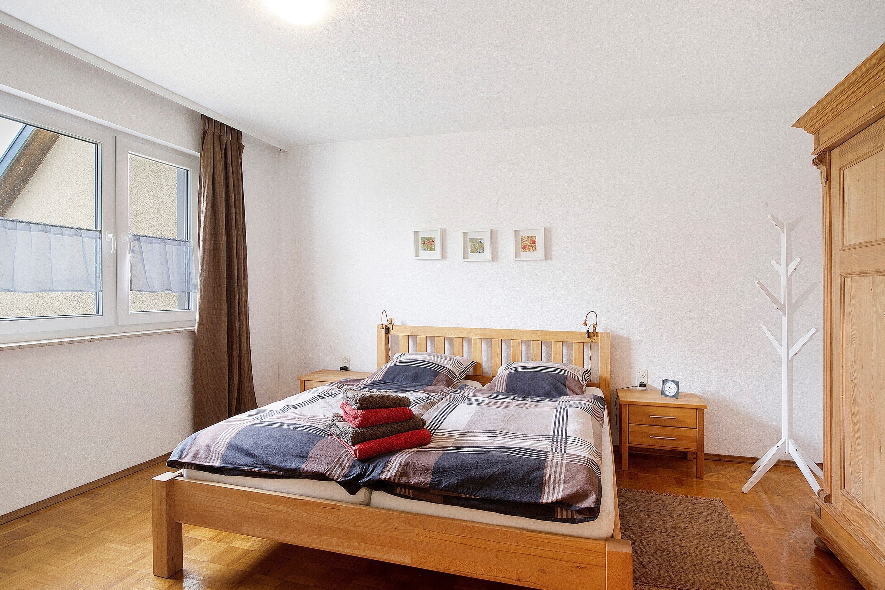 Une chambre à coucher avec un lit en bois, une table de chevet, un porte-manteau et une fenêtre avec des rideaux.