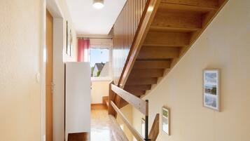 A wooden staircase with a handrail, a door on the left, and a window with a view of buildings outside.