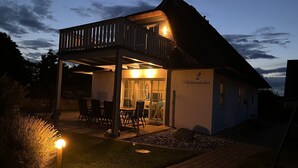 En toetages bygning med balkon, et spiseområde med stole og et bord, og et skilt der viser '2 Achternkater'.